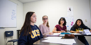 Four students sitting at a table with one student talking and gesturing.