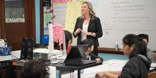 An educator teaches to a room of middle schoolers from the front of the classroom.