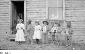 Young boys in top hats and girls in dresses are standing in a line, each holding up a letter. 