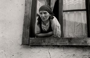 A woman wearing a scarf on her head leans out of a window. Photo taken circa 1935-1938.
