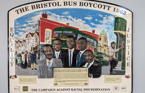 A commemorative plaque of the Bristol Bus Boycott showing a red building, a bus, and several people.