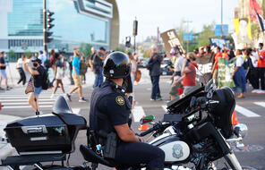 Police officer monitoring protestors on motorcycle.