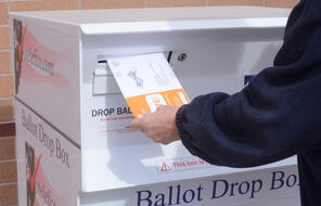 Hand putting Jefferson County Colorado election ballot envelope into ballot drop box in early voting mail election