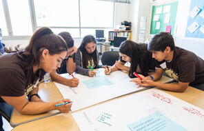 Group of students writing on large piece of chart paper.