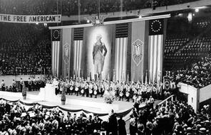 Hundreds of people at the German American Bund Rally look at the main stage with American Flags and an image of George Washington.