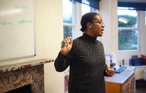 An educator of color speaks with a green marker in hand.