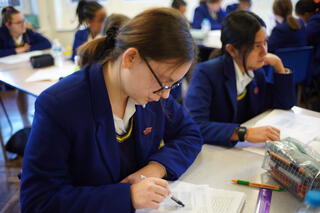 Uniformed high school students write at their desks.