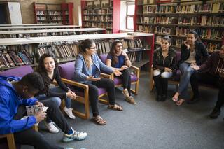 Students sit in a circle in a library and smile and laugh