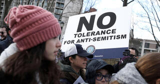 A person stands with a sign that reads "No Tolerance for Anti-Semitism."