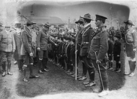 Men in uniforms surround a line of young Boy Scouts. 