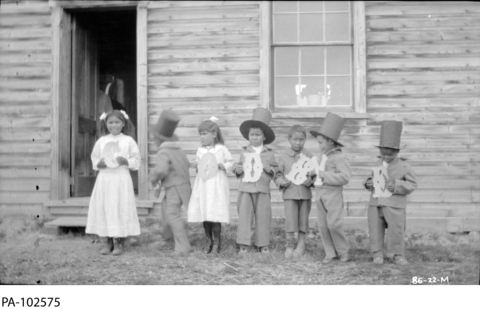 Young boys in top hats and girls in dresses are standing in a line, each holding up a letter. 