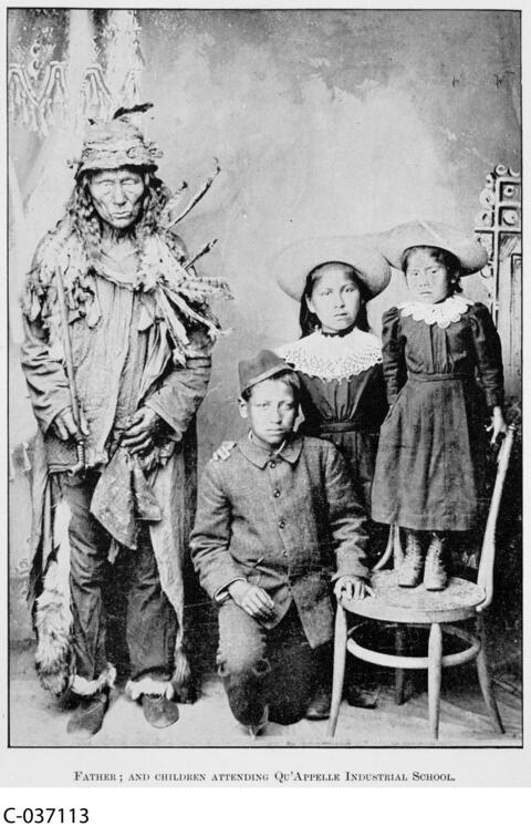 Man in traditional indigenous attire and three children in western dresses and pants. 