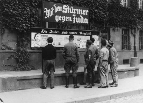 An issue of the antisemitic propaganda newspaper Der Stürmer (The Attacker) is posted on the sidewalk in Worms, Germany, in 1935. The headline above the case says, ""The Jews Are Our Misfortune.""