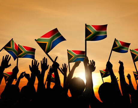 Group of people waving South African flags in back lit.