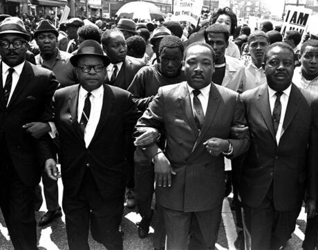Photo of Martin Luther King, Jr. marching arm in arm with a crowd of men participating in the  1968 Memphis Sanitation Worker's Strike.