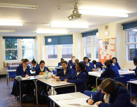 Uniformed school students complete assignments at their desks. 