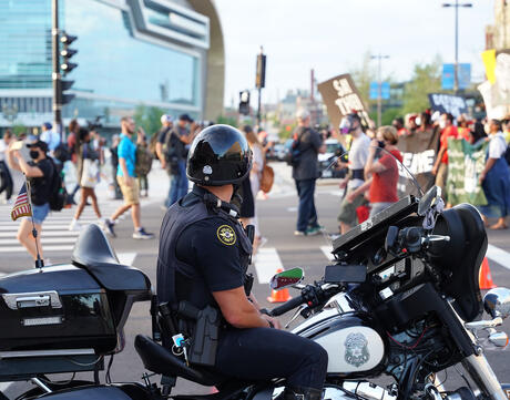 Police officer monitoring protestors on motorcycle.