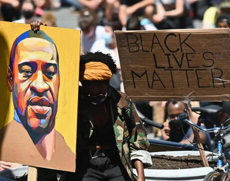 A protester holding a painting of George Floyd and a sign that reads "Black Lives Matter"
